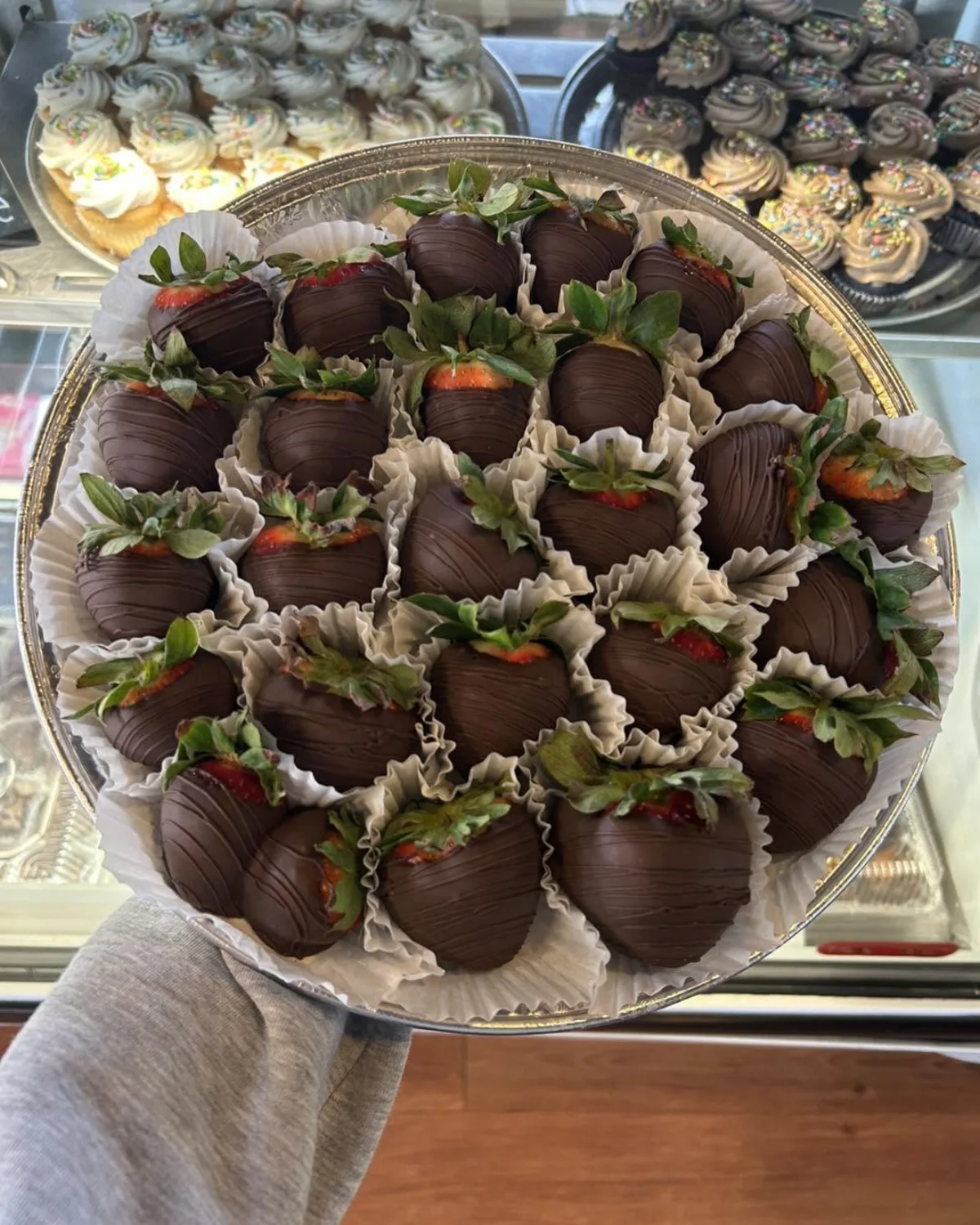 A tray of chocolate covered strawberries held up in front of the bakery case