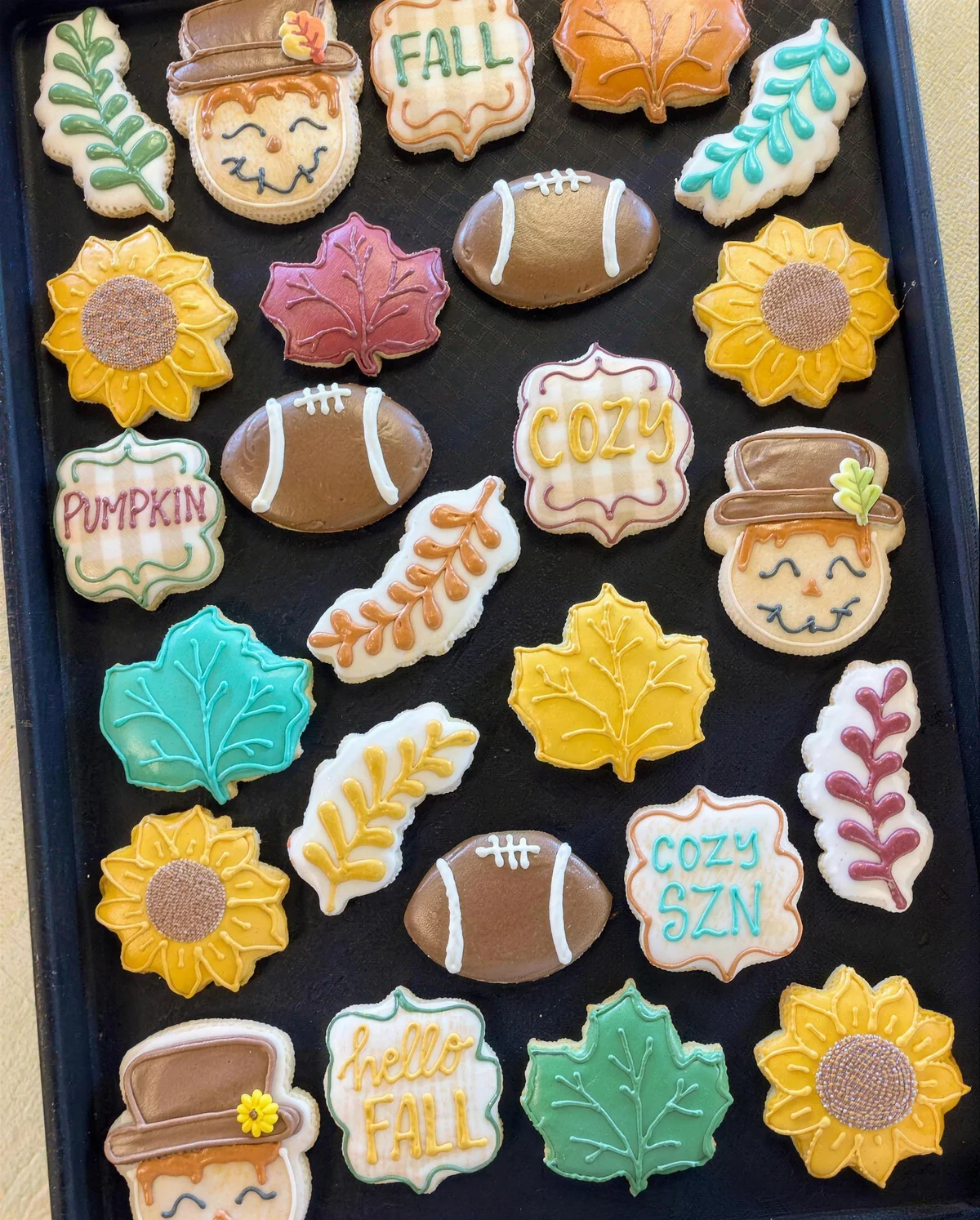 A tray of hand decorated fall sugar cookies: sunflowers, leaves, footballs and scarecrows