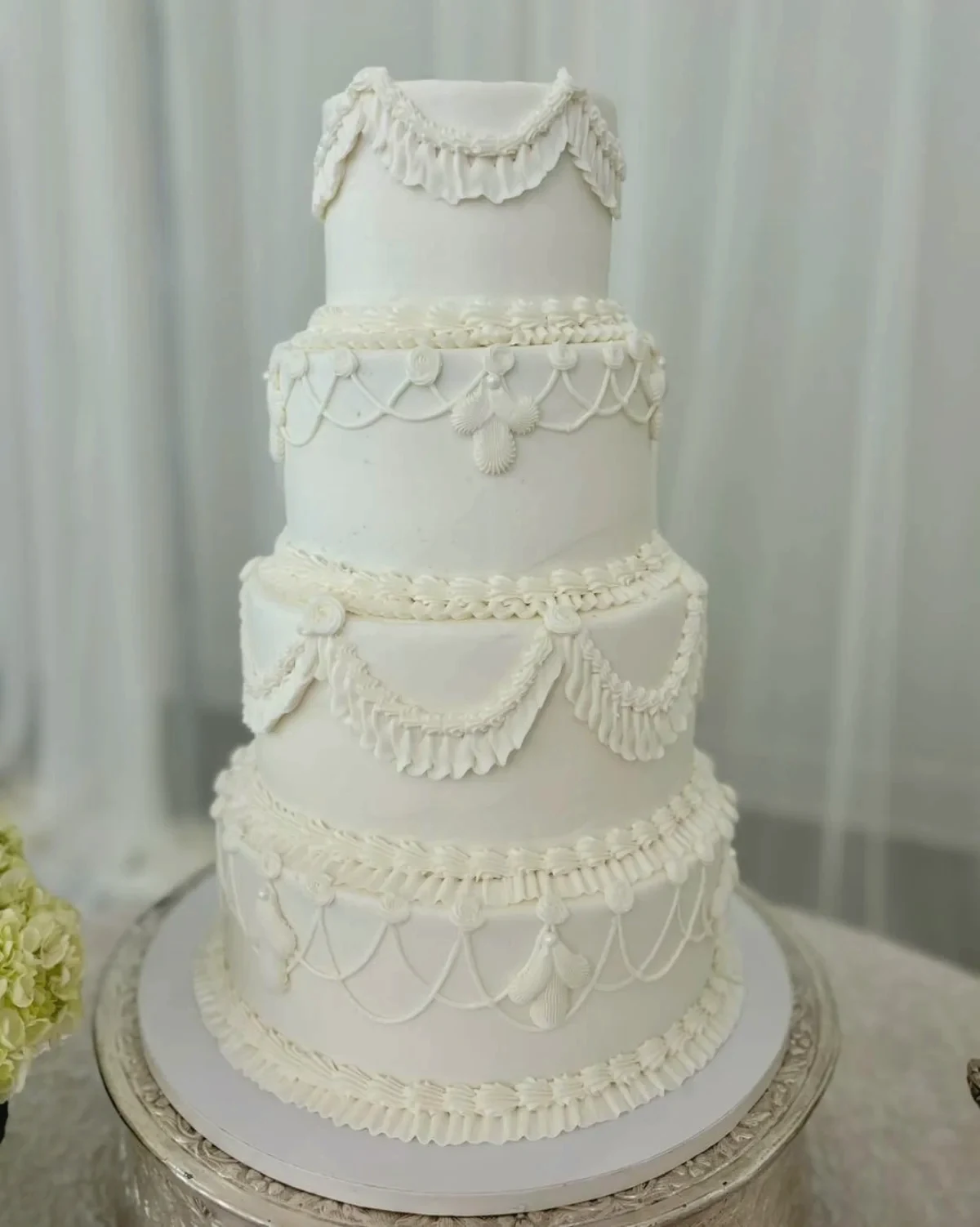 A four-tier wedding cake with piped swags and pearls