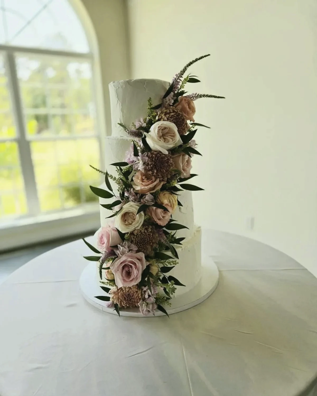 A tall wedding cake with a cascade of dried and fresh flowers