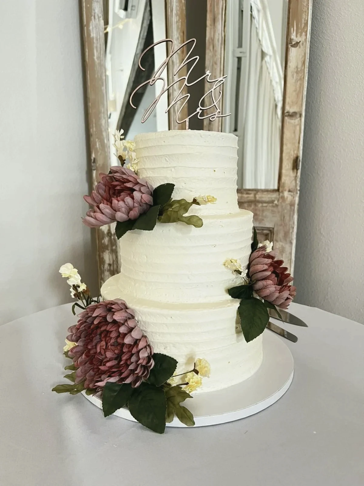 A tiered cake with deep pink mums and a mirror